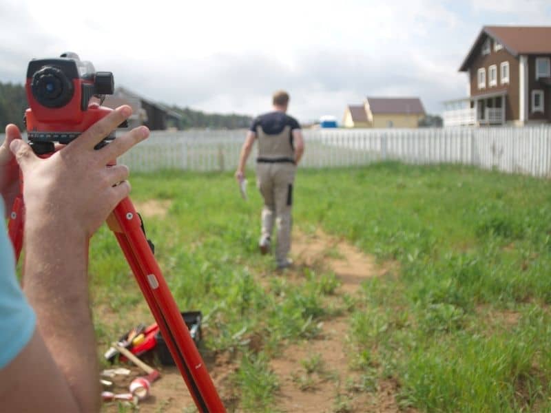 Land surveyors locating property boundaries near a residential fence before replacing an existing fence.